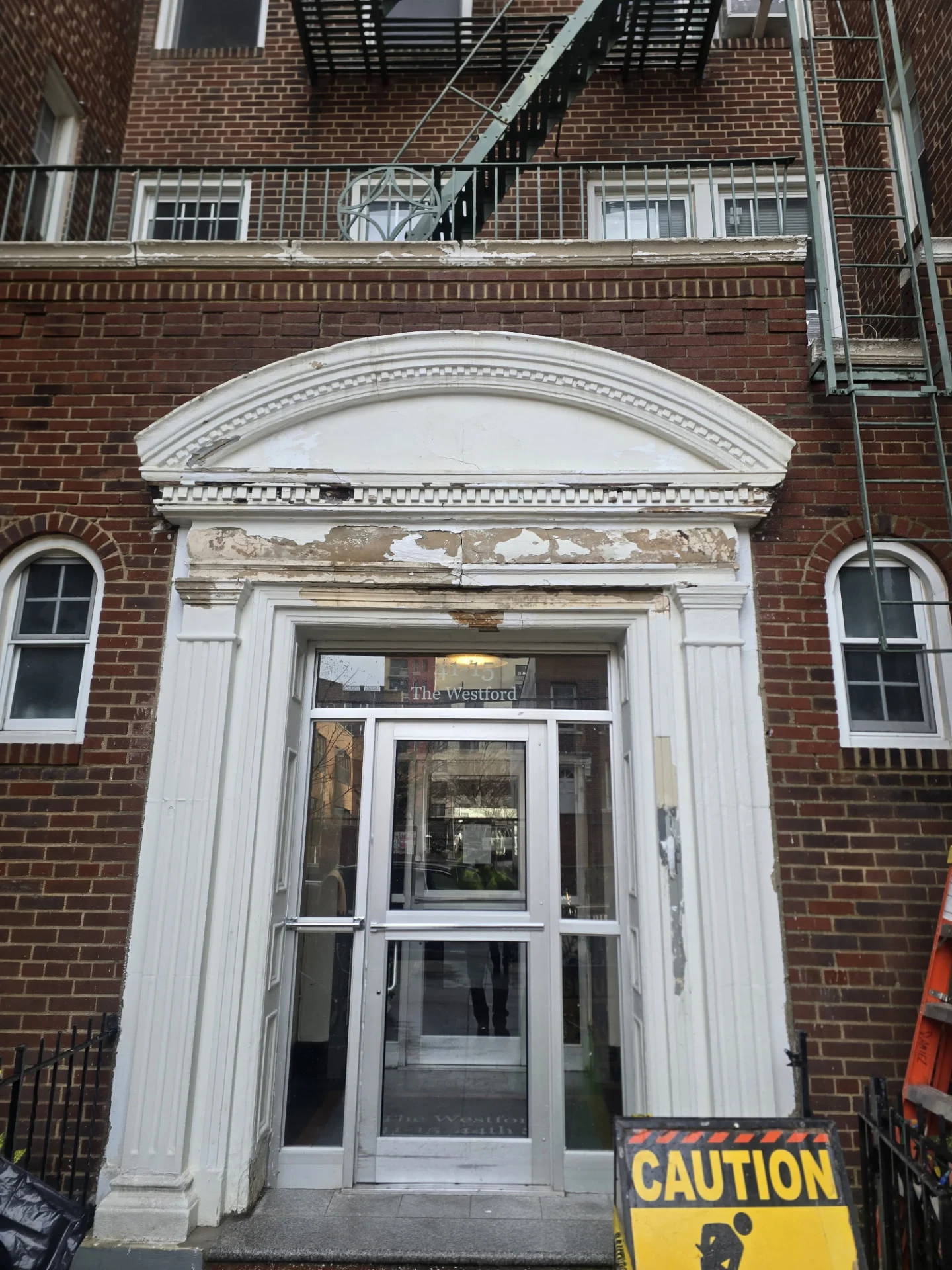 Building entrance before restoration: damaged white architectural molding and peeling paint on brick facade